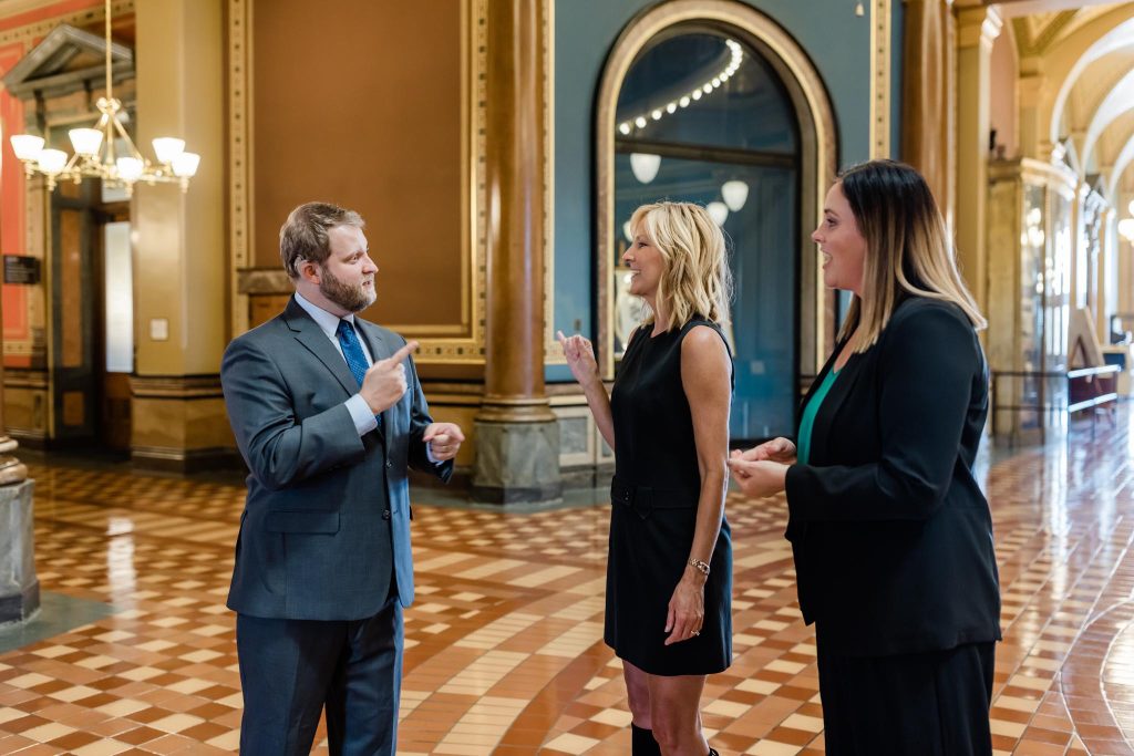 Three business professionals communicate through signing in a courthouse hallway